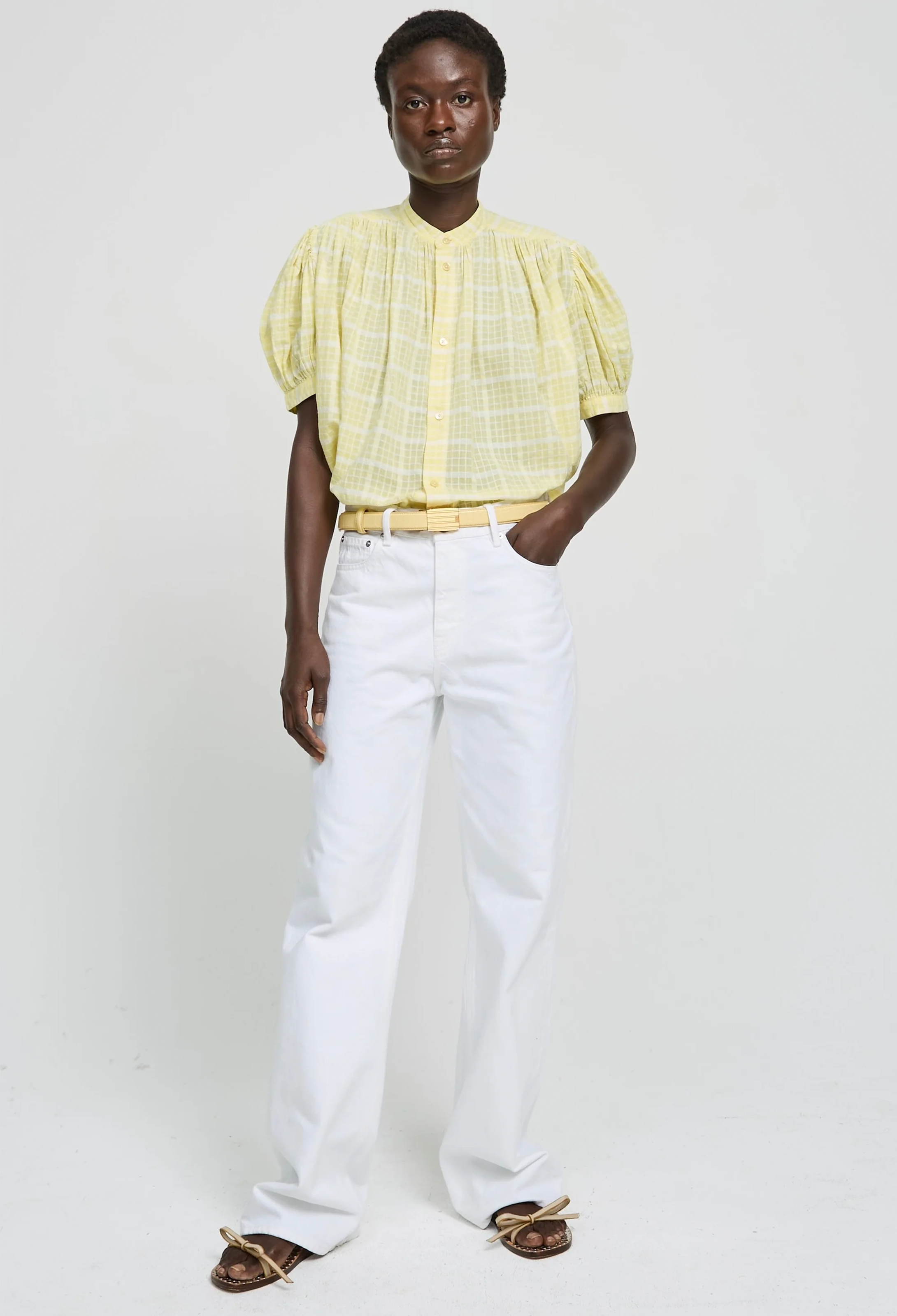 Person wearing a yellow blouse and white pants on a plain background