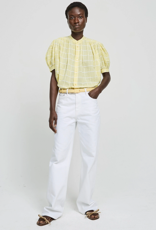 Person wearing a yellow blouse and white pants on a plain background