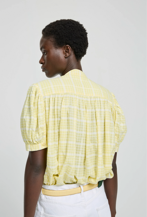 Person wearing a yellow checkered blouse against a white background