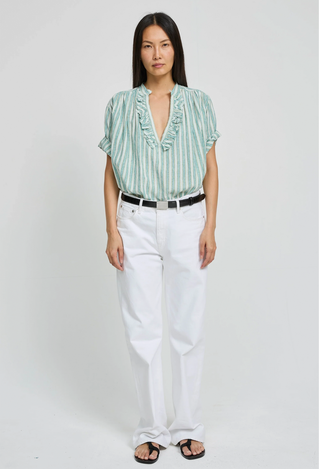 Woman wearing a green striped shirt and white pants on a plain background