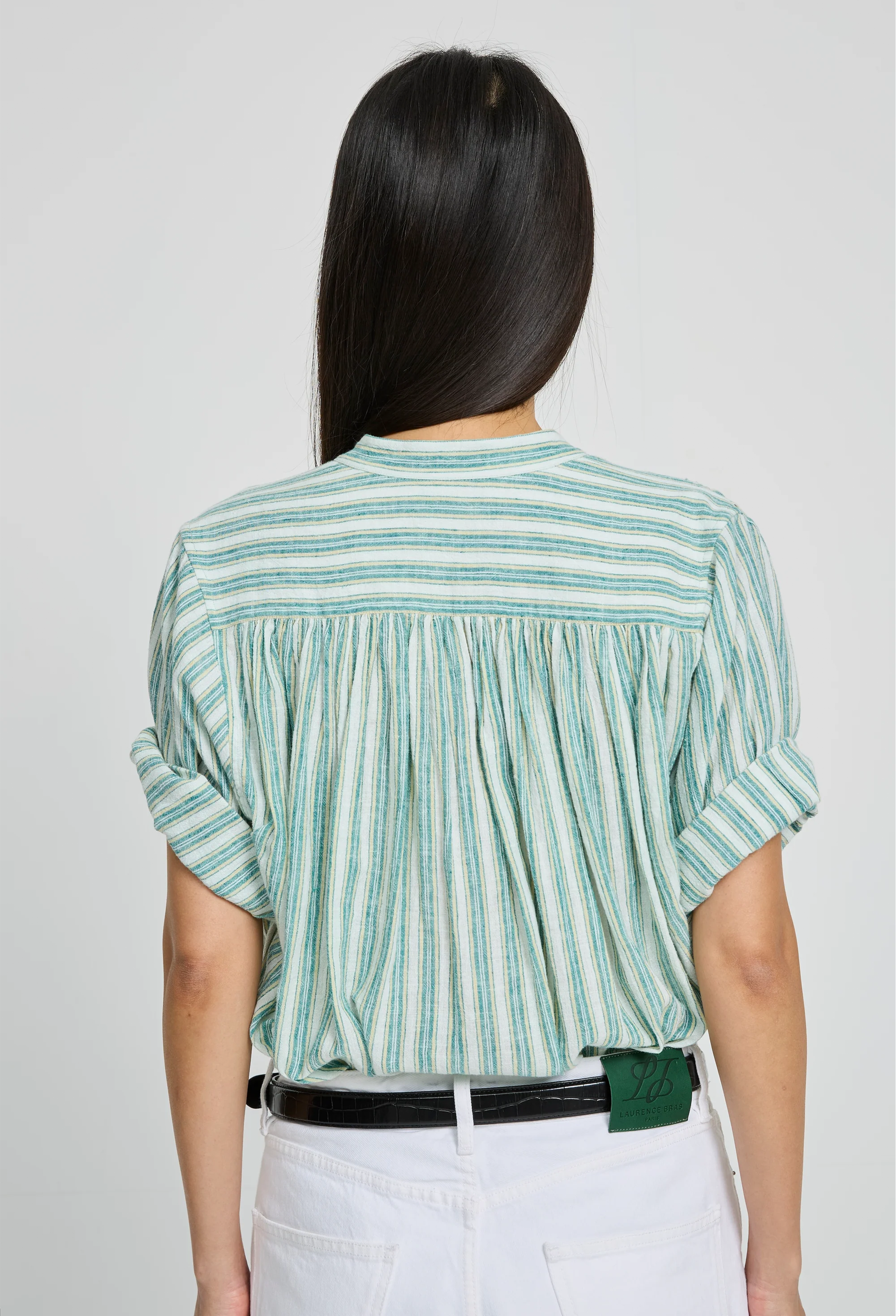 Person wearing a green and white striped shirt with rolled-up sleeves on a plain background