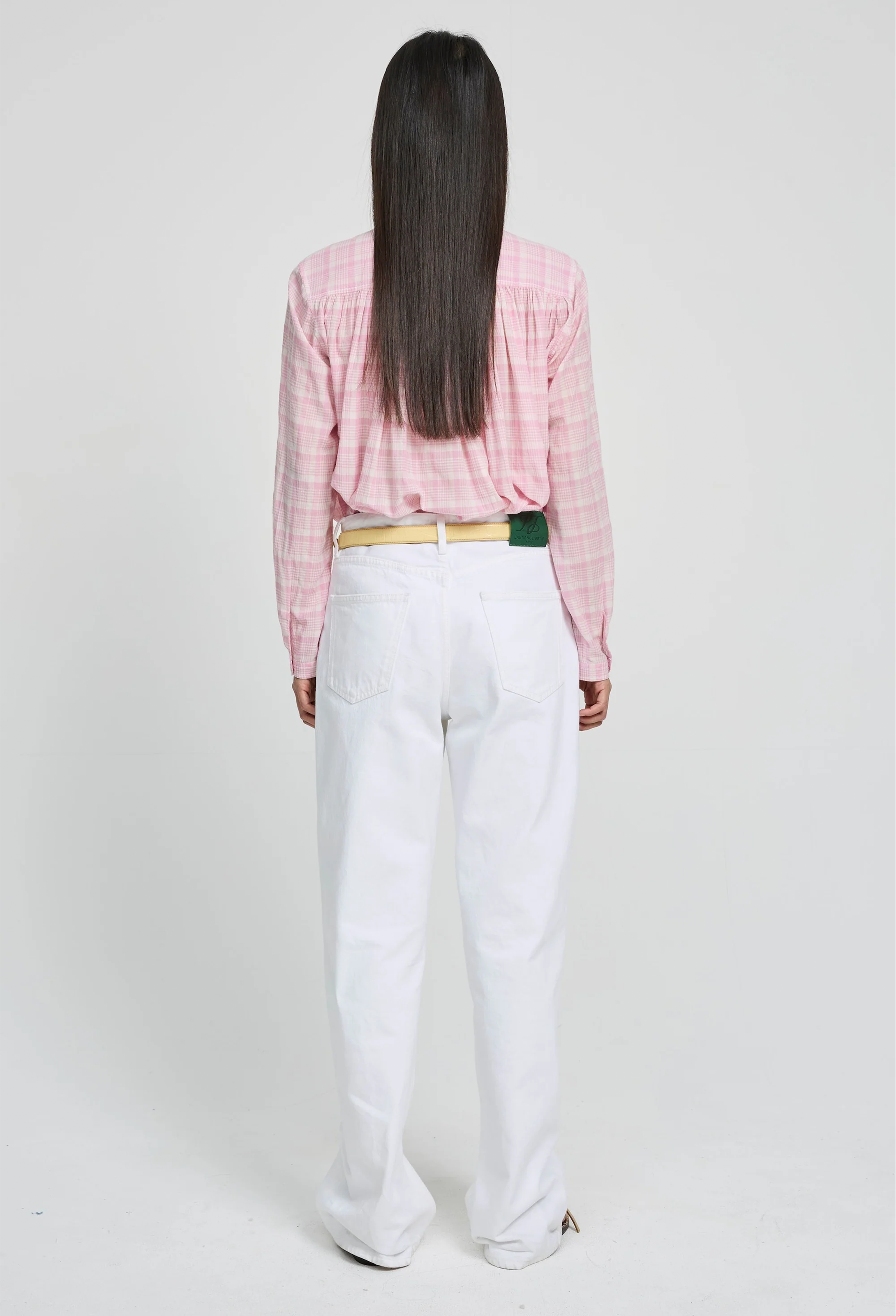 Person wearing a pink plaid shirt and white pants on a white background