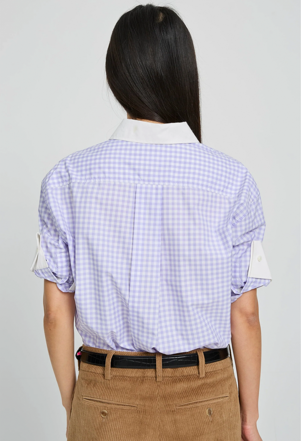 Person wearing a light purple checkered shirt with rolled-up sleeves on a plain background