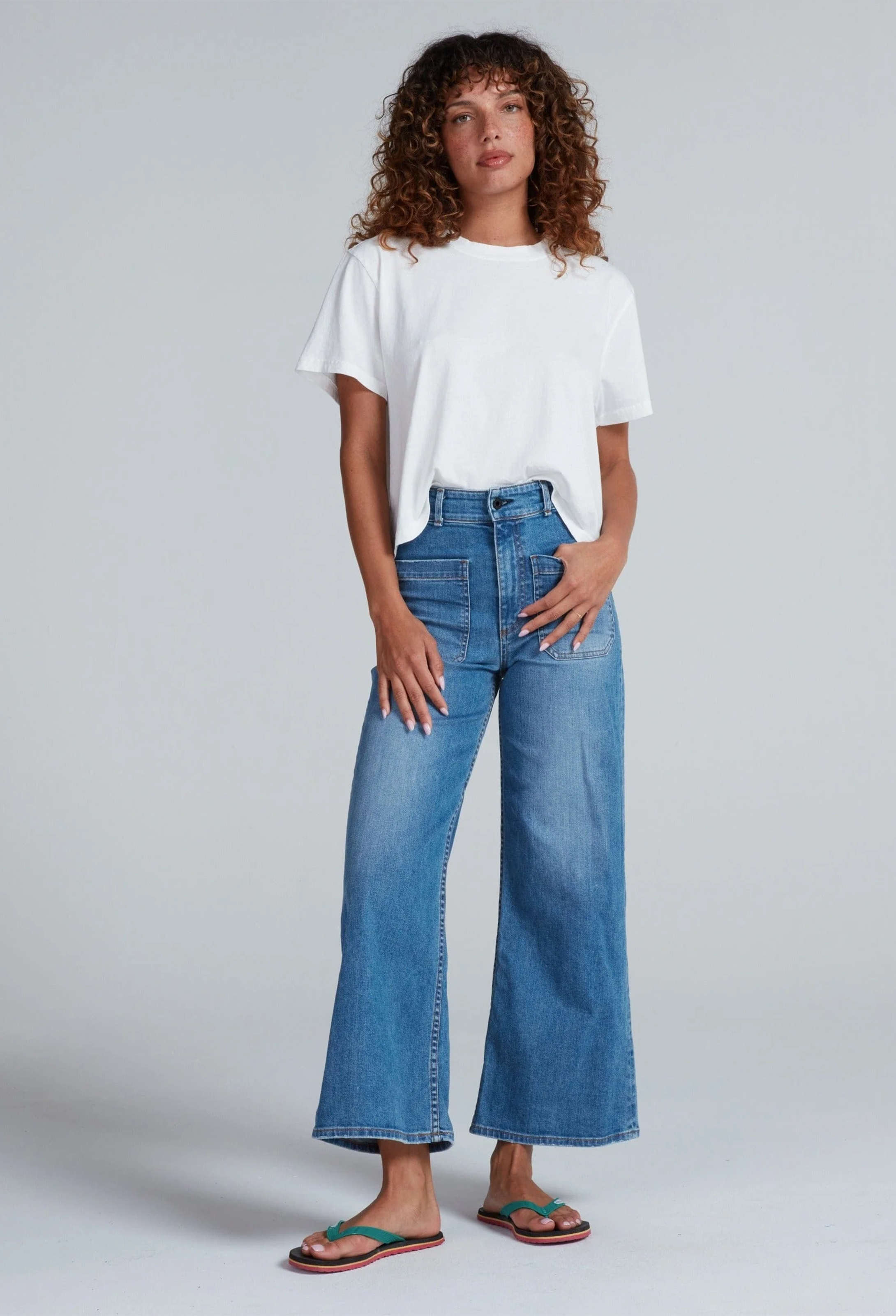 Woman wearing a white t-shirt and blue jeans on a plain background
