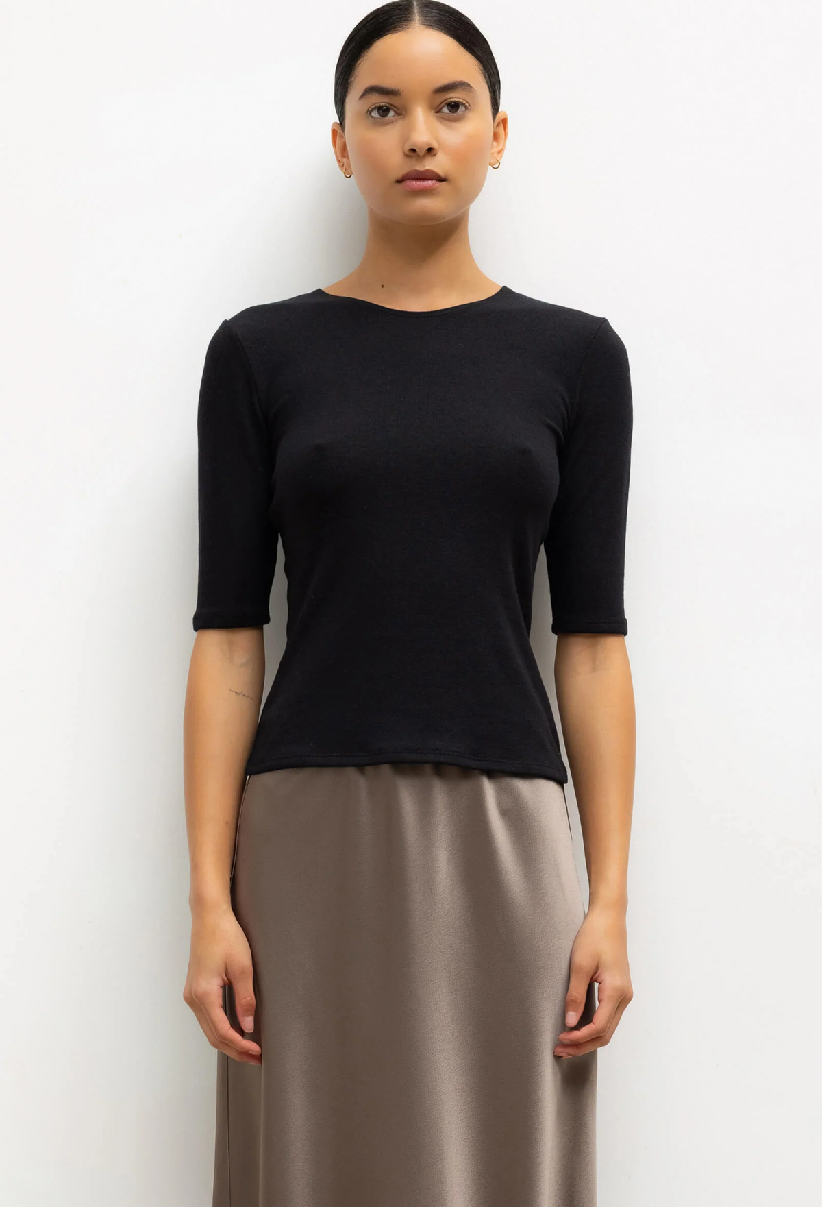 Woman wearing a black top and beige skirt against a white background