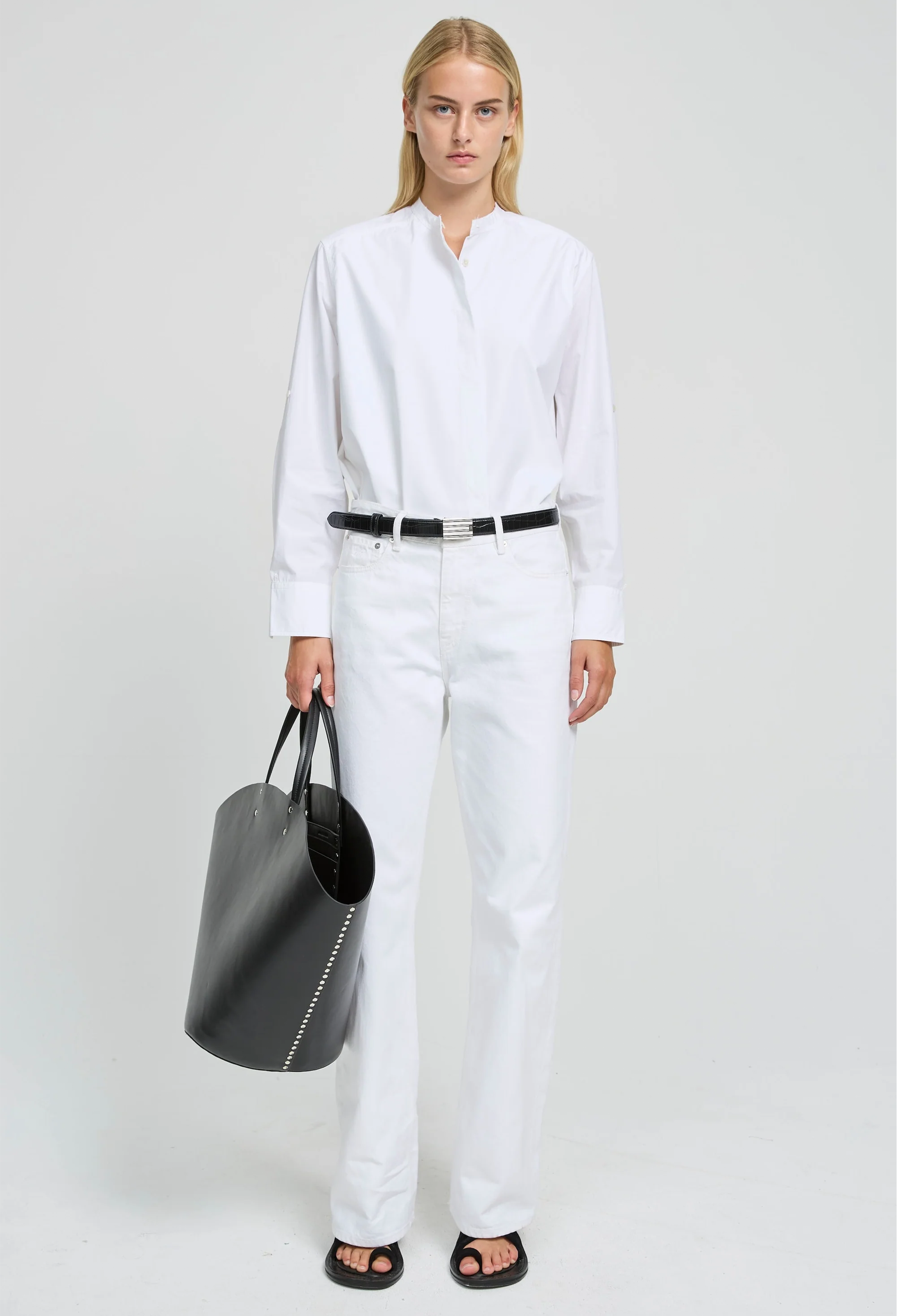 Person wearing a white shirt and pants holding a black bag on a white background
