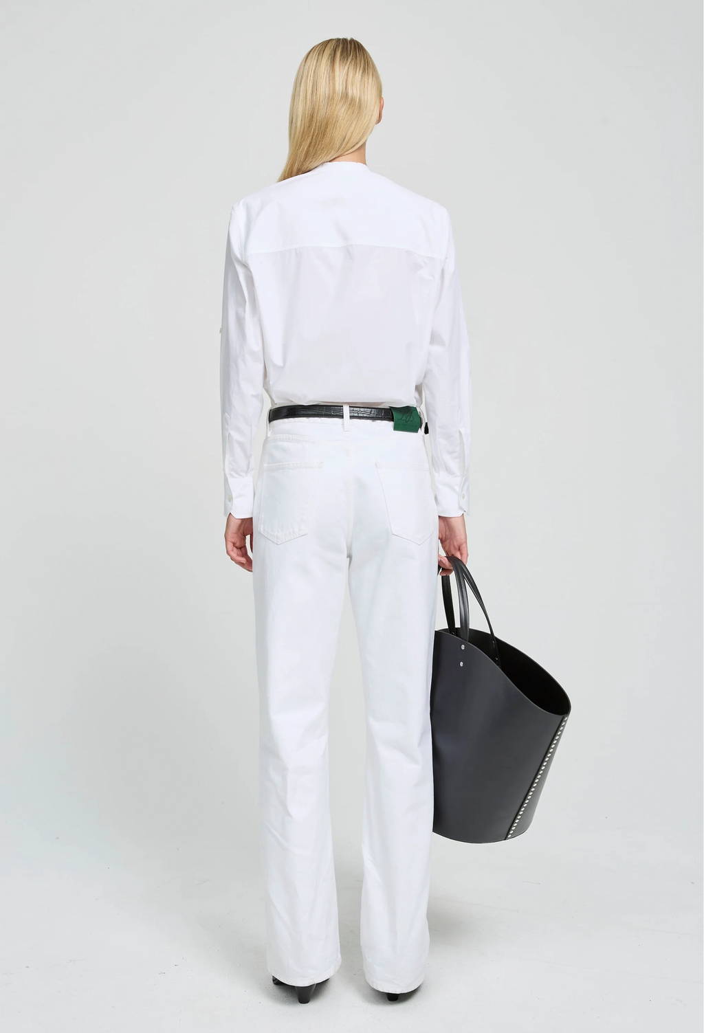 Person wearing a white outfit holding a black bag on a plain background