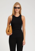 Woman wearing a black sleeveless top and black pants, holding a brown leather clutch against a white background.