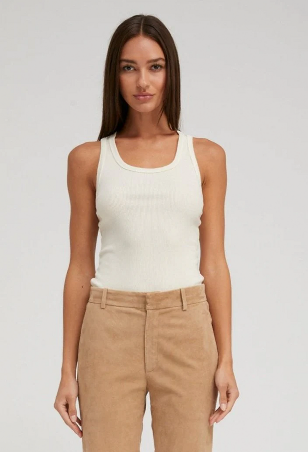 Woman wearing a creme tank top and beige pants on a plain background