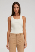 Woman wearing a creme tank top and beige pants on a plain background