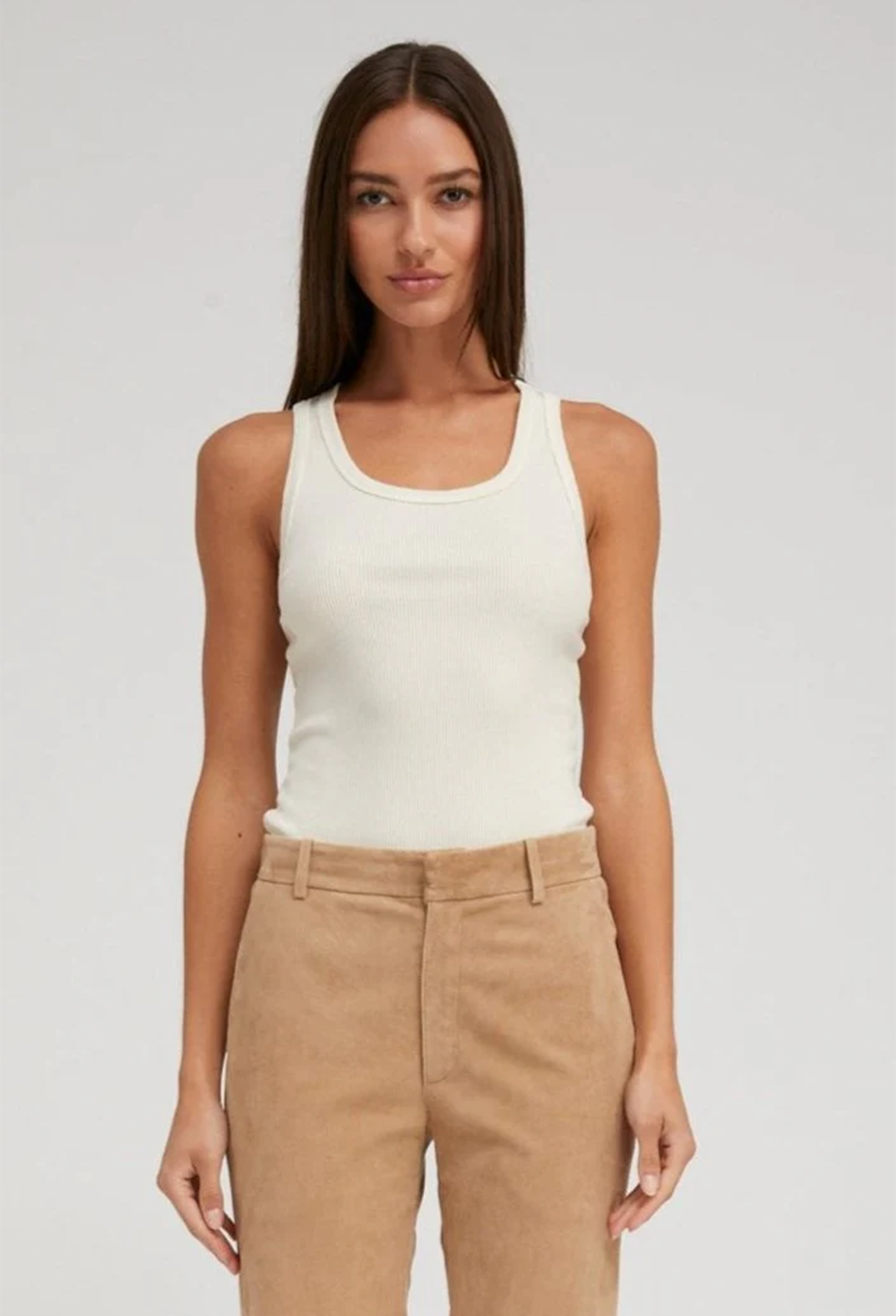 Woman wearing a creme tank top and beige pants on a plain background