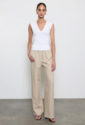 Woman wearing a white sleeveless top and beige pants against a plain background