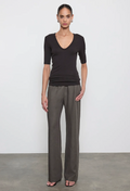 Woman wearing a black top and gray pants against a white background