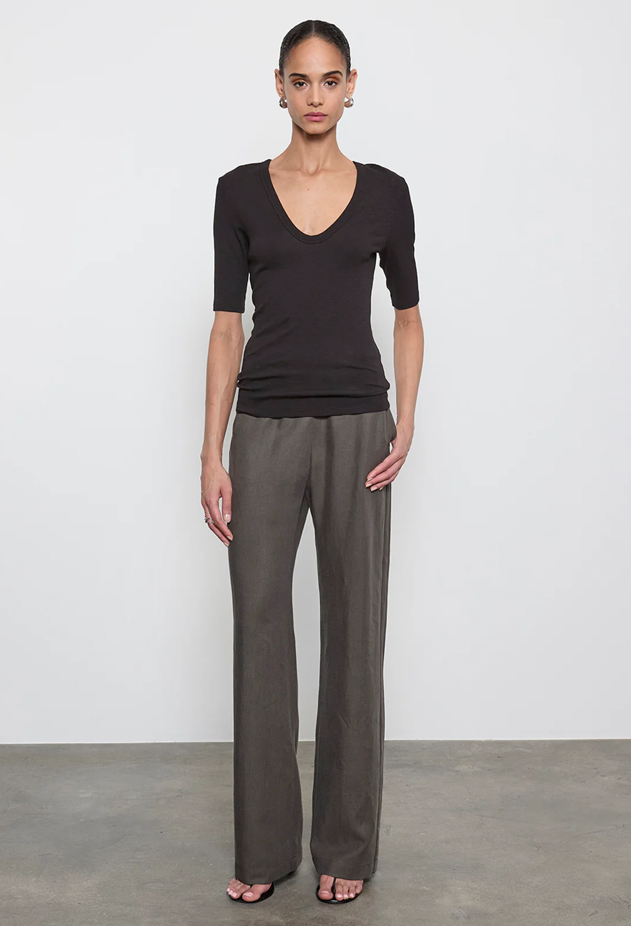 Woman wearing a black top and gray pants against a white background