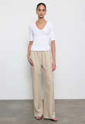 Woman wearing a white top and beige pants against a plain background
