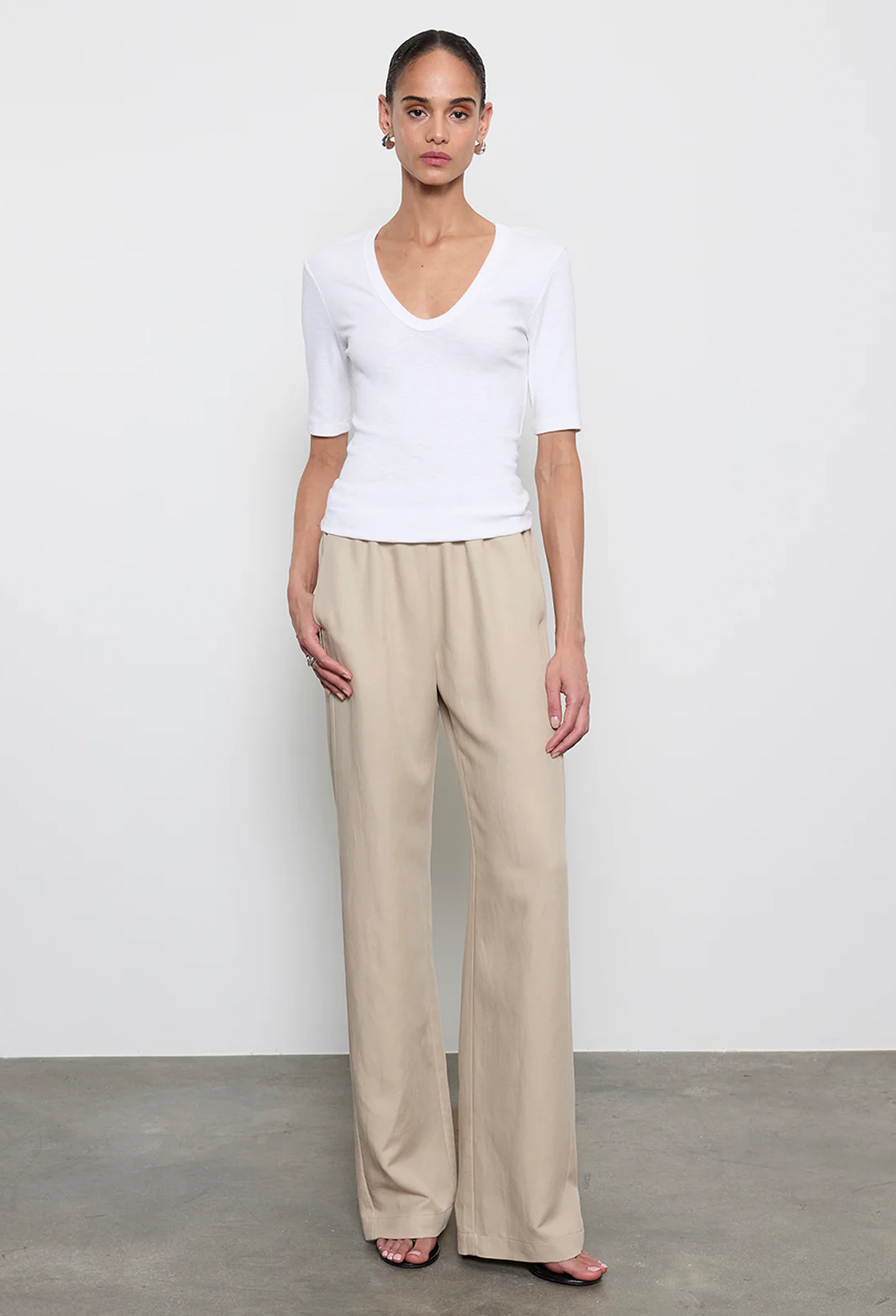 Woman wearing a white top and beige pants against a plain background