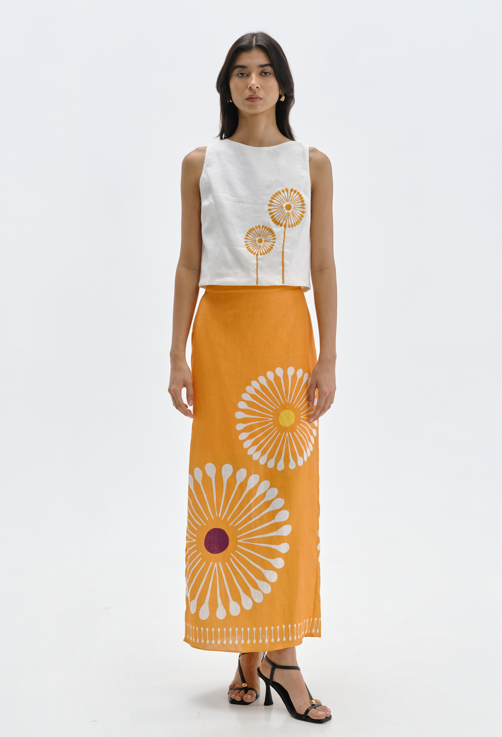Woman wearing a white sleeveless top with floral design and an orange skirt with similar floral pattern on a white background