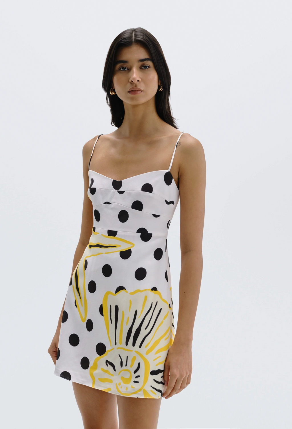 Woman wearing a white dress with black polka dots and yellow floral patterns on a plain background