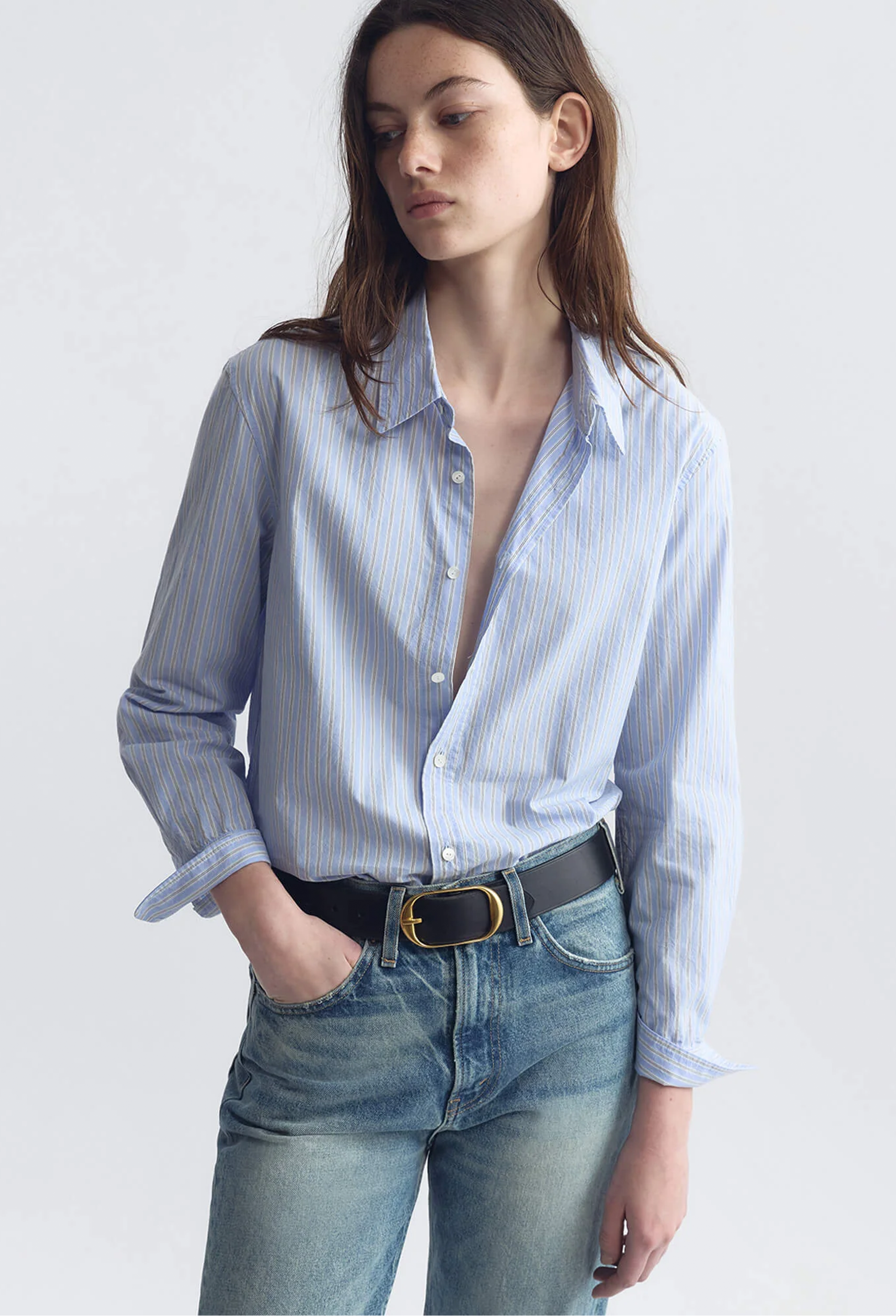 Woman wearing a light blue striped shirt and jeans on a white background