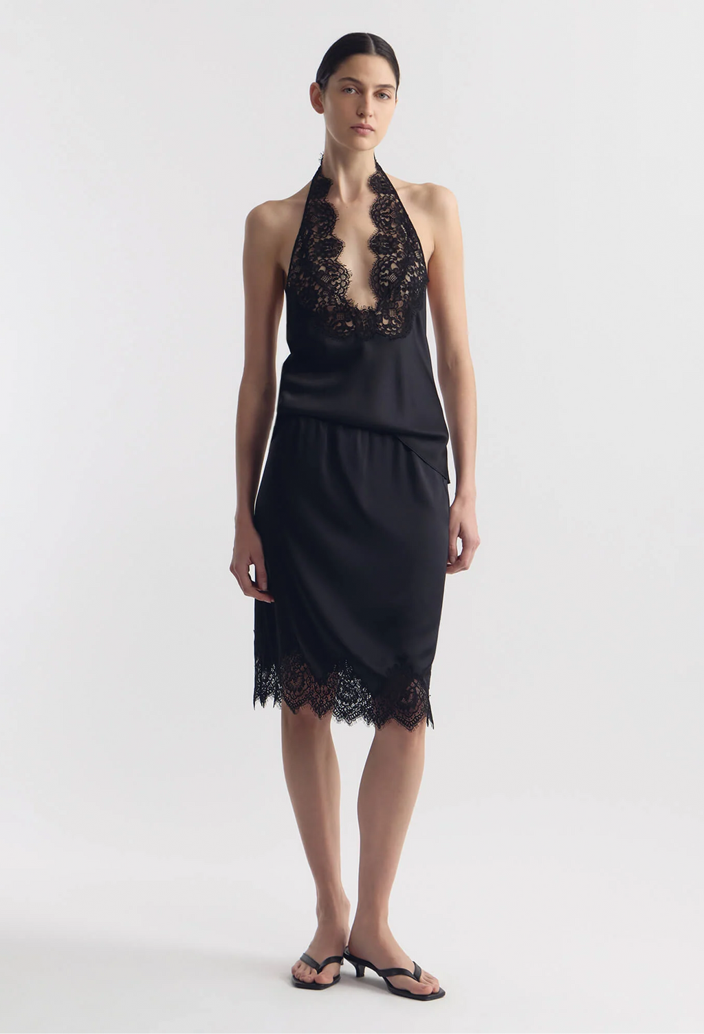 model wearing a black silk tank and matching skirt with lace hem on a white background