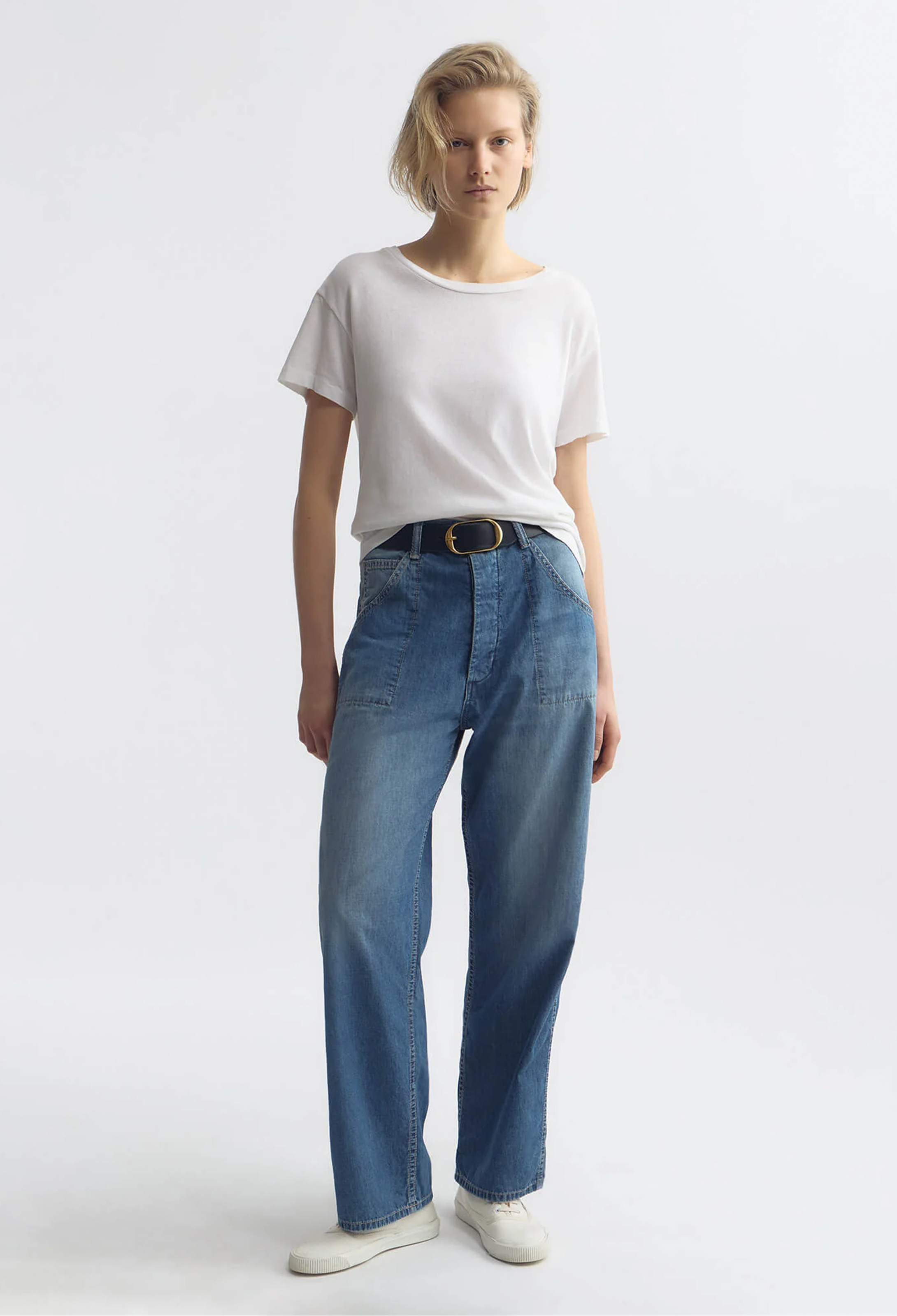 Person wearing a white t-shirt and blue jeans on a plain background