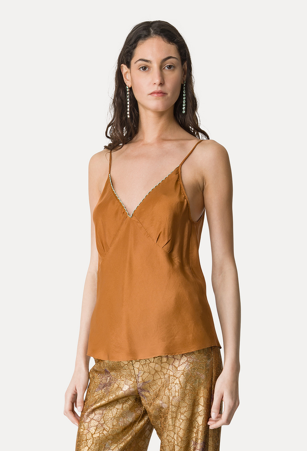 Woman wearing a mustard yellow satin top and gold pants on a white background