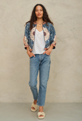 Woman wearing a floral jacket, white top, and blue jeans against a beige background