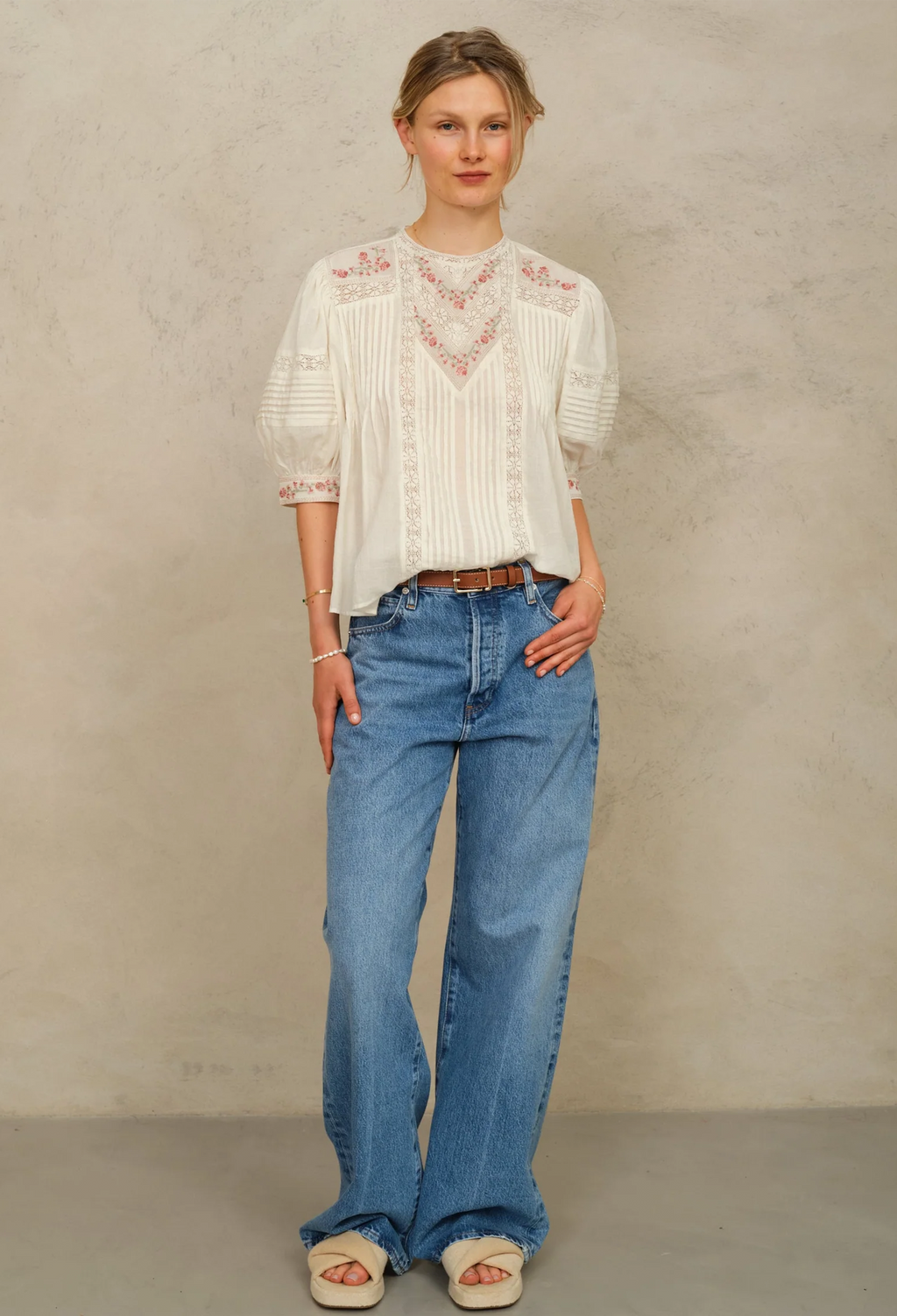 Woman wearing a white blouse with lace details and blue jeans against a beige background