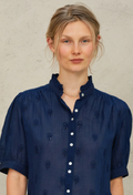 Woman wearing a navy blue blouse with white buttons against a neutral background
