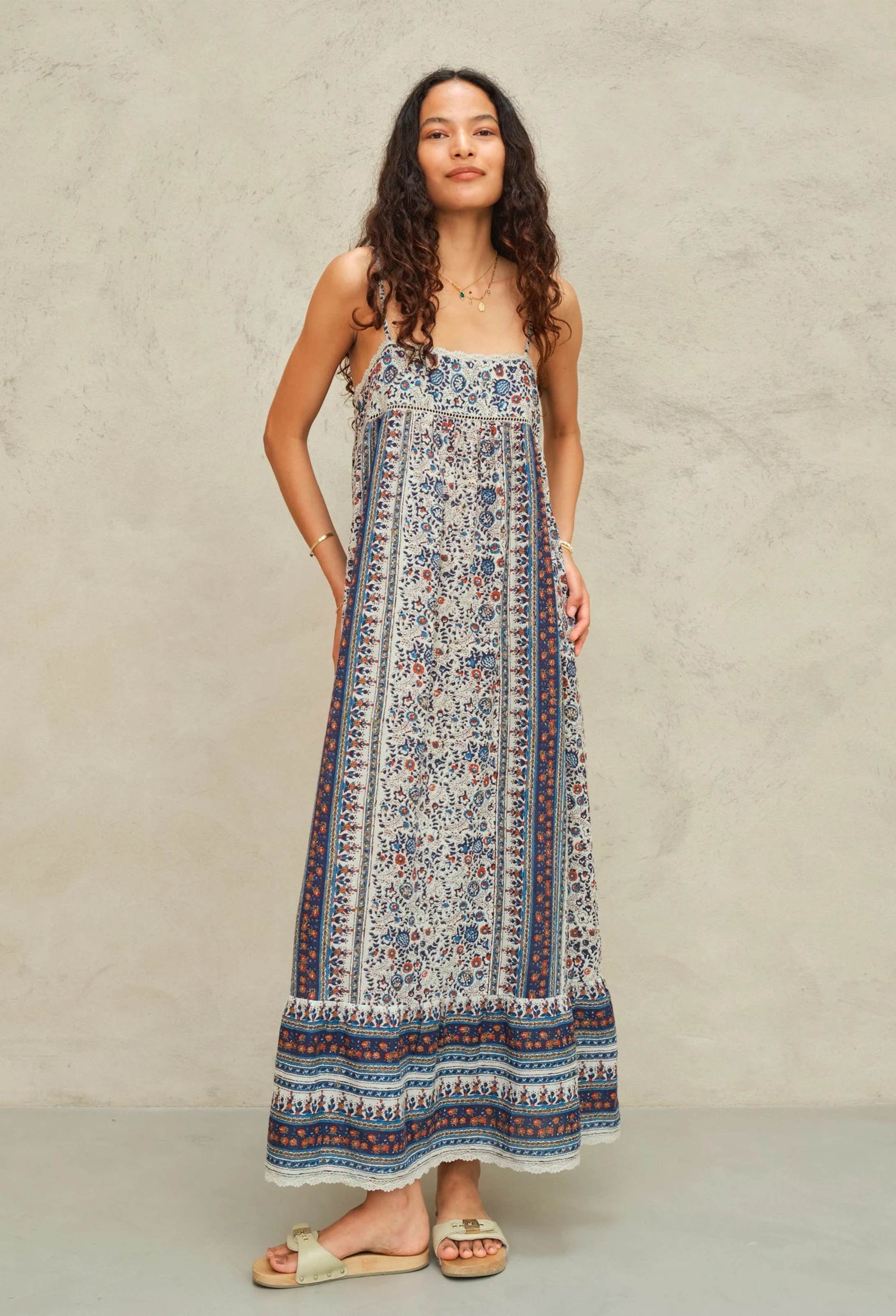 Woman wearing a long, patterned dress against a plain background