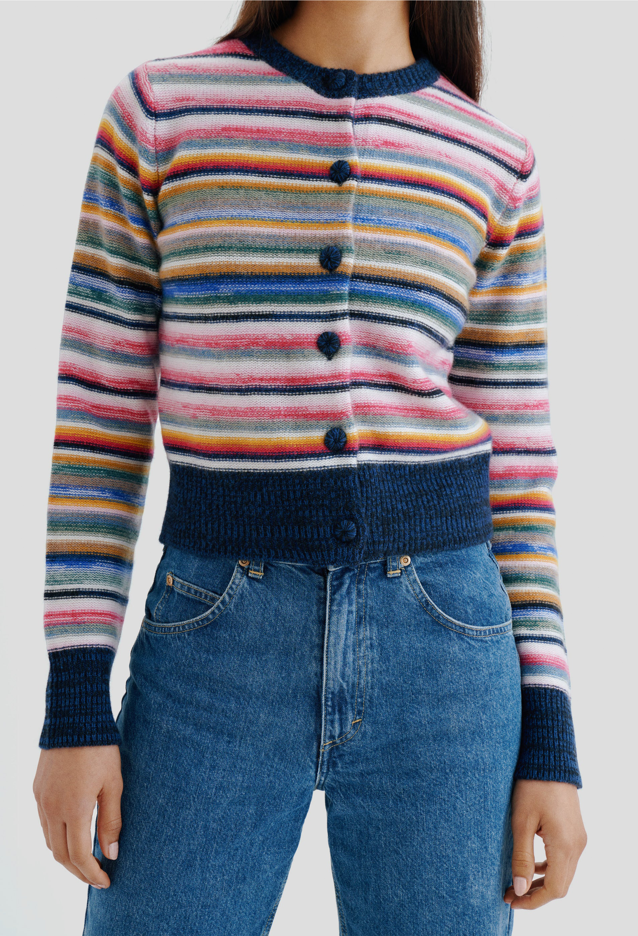 Multicolored striped sweater with buttons worn by a person, paired with blue jeans on a plain background.