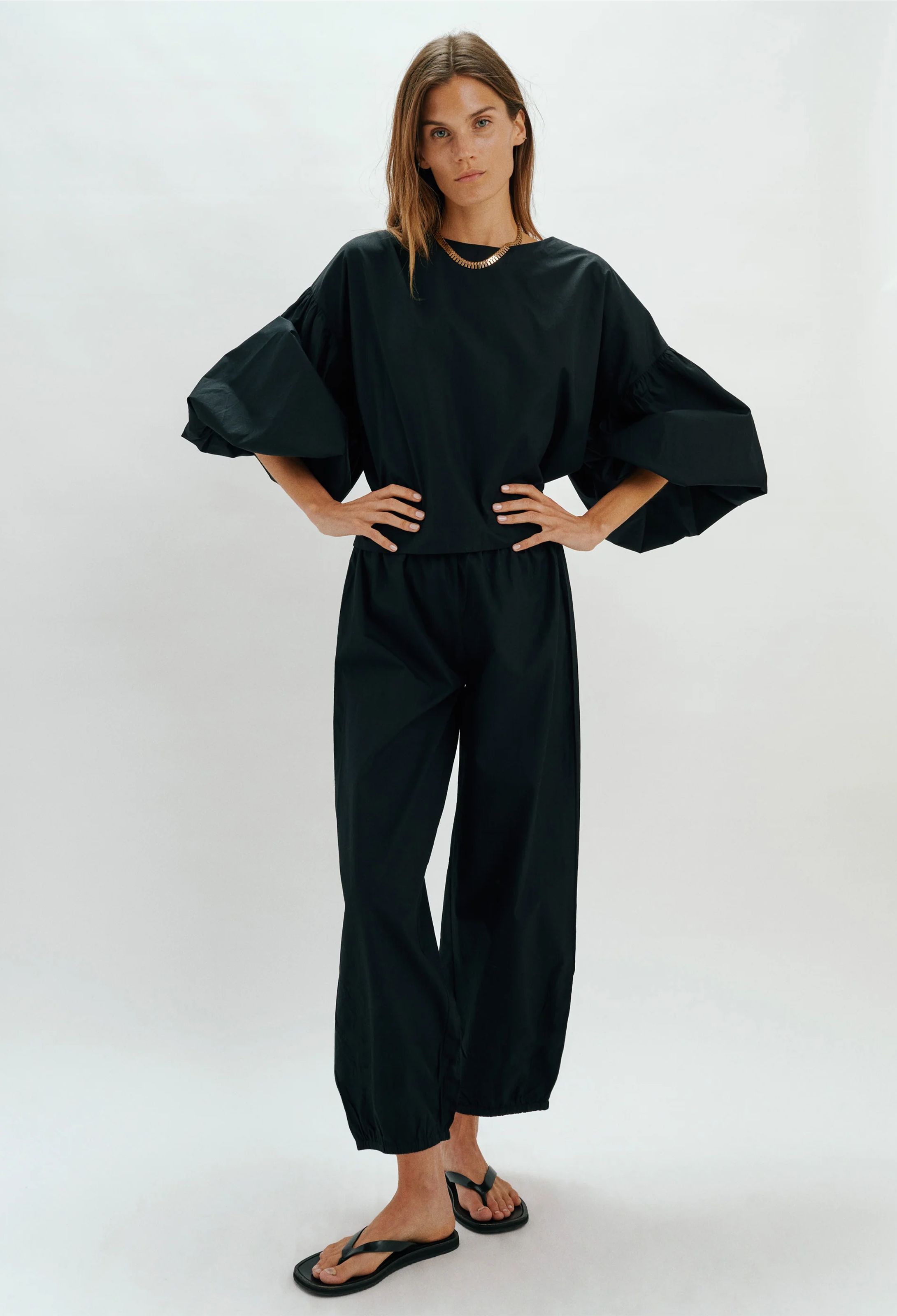 Person wearing a black outfit with wide sleeves on a white background