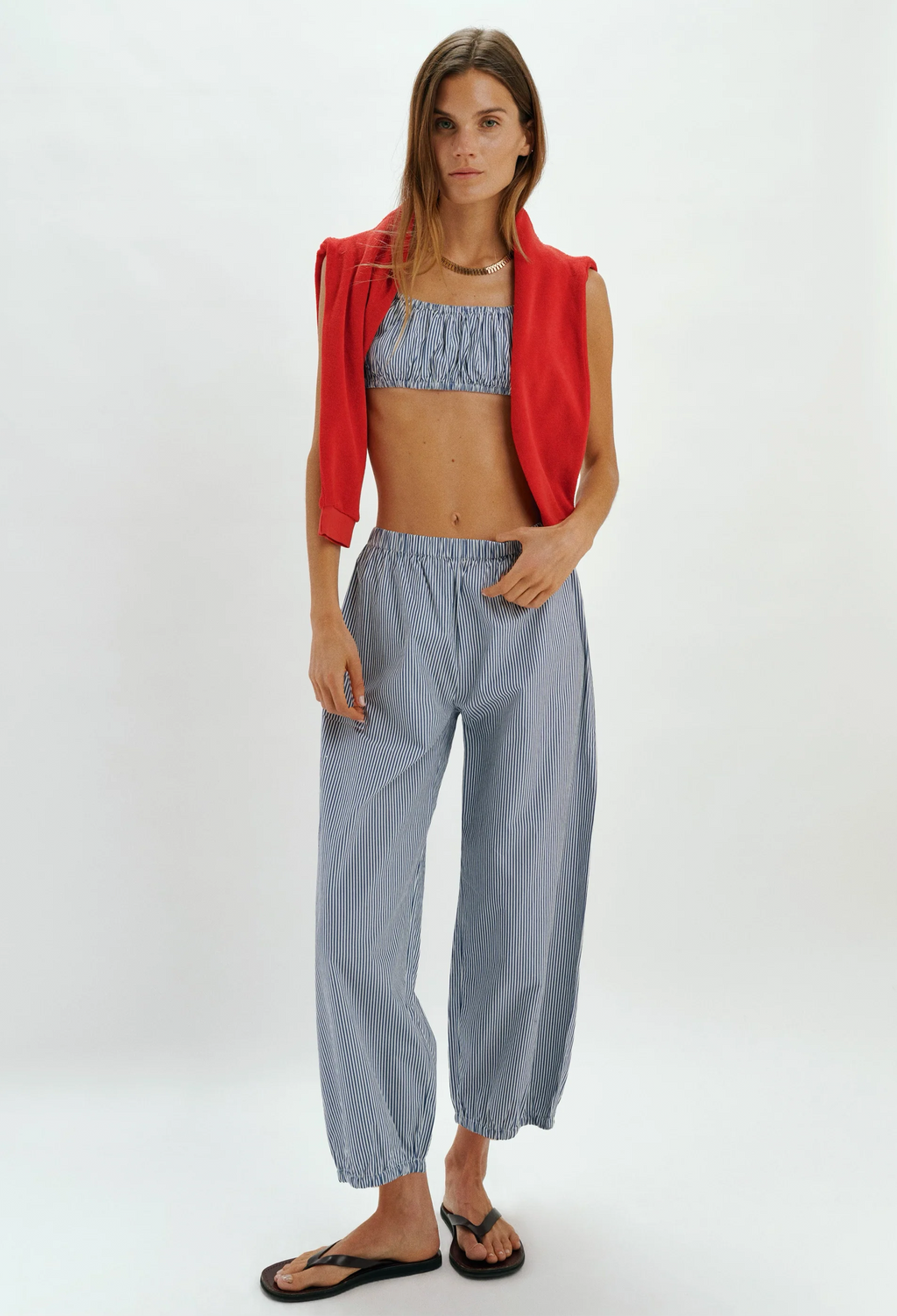 Woman wearing a red jacket, blue patterned top, and light blue pants on a white background
