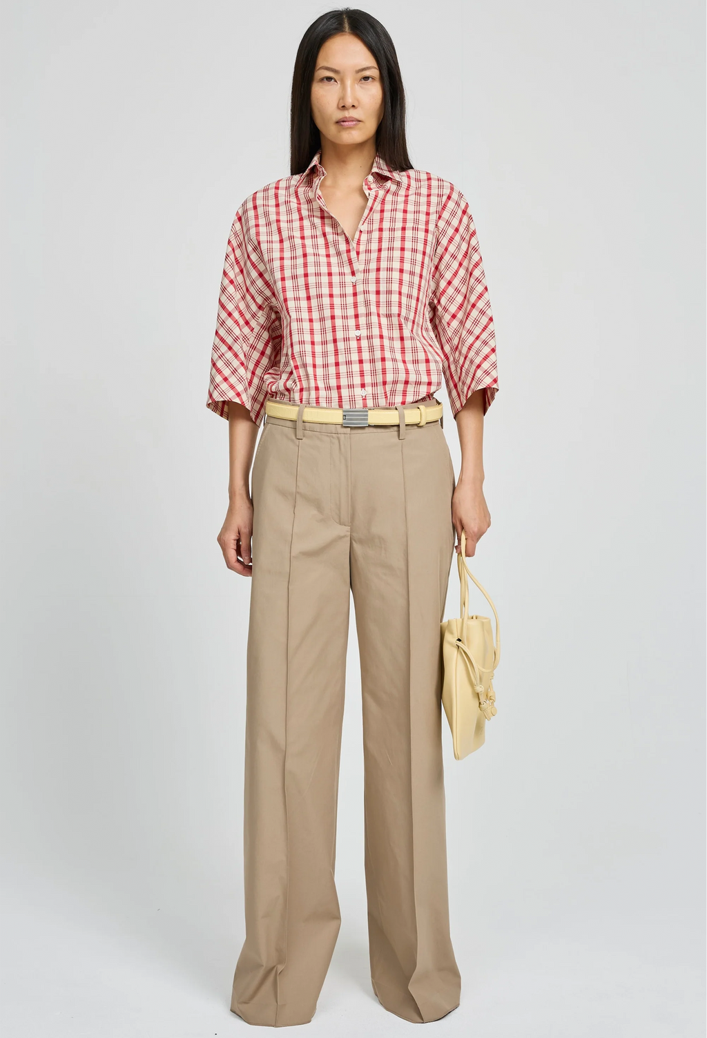 Woman wearing a red and white checkered shirt with beige pants on a white background