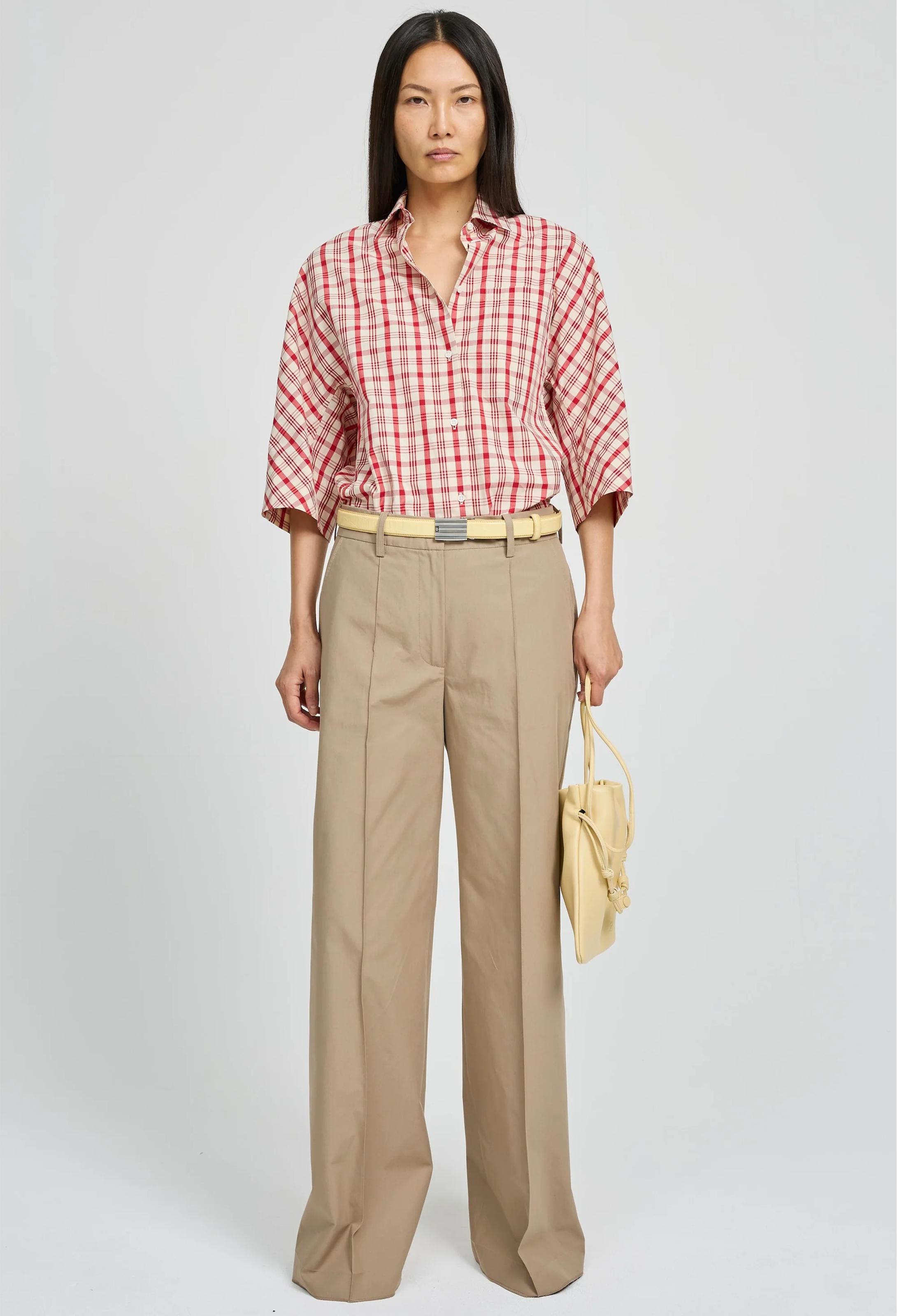 Woman wearing a red and white checkered shirt with beige pants on a white background