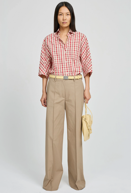 Woman wearing a red and white checkered shirt with beige pants on a white background