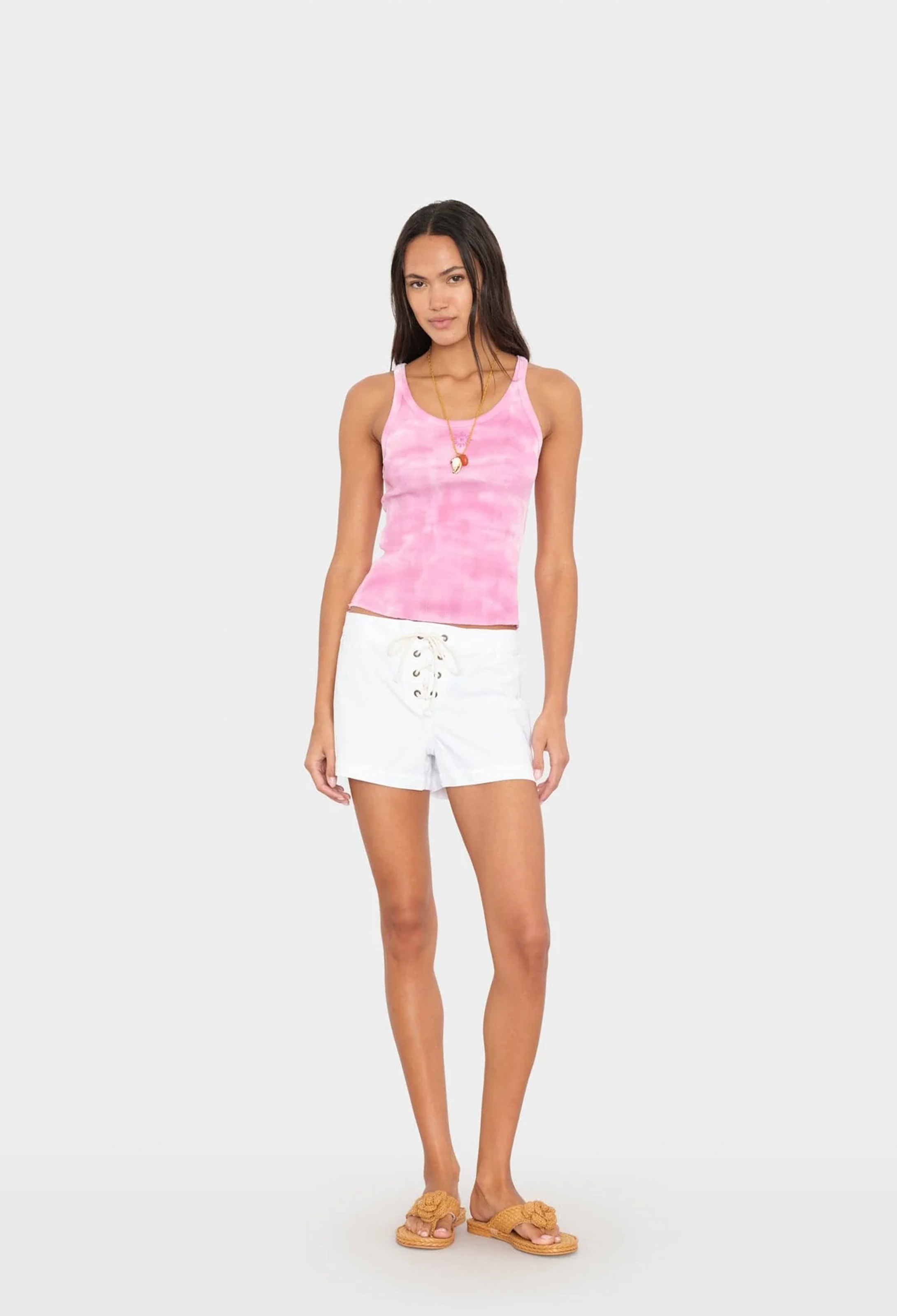 Woman wearing a pink tank top and white shorts on a white background