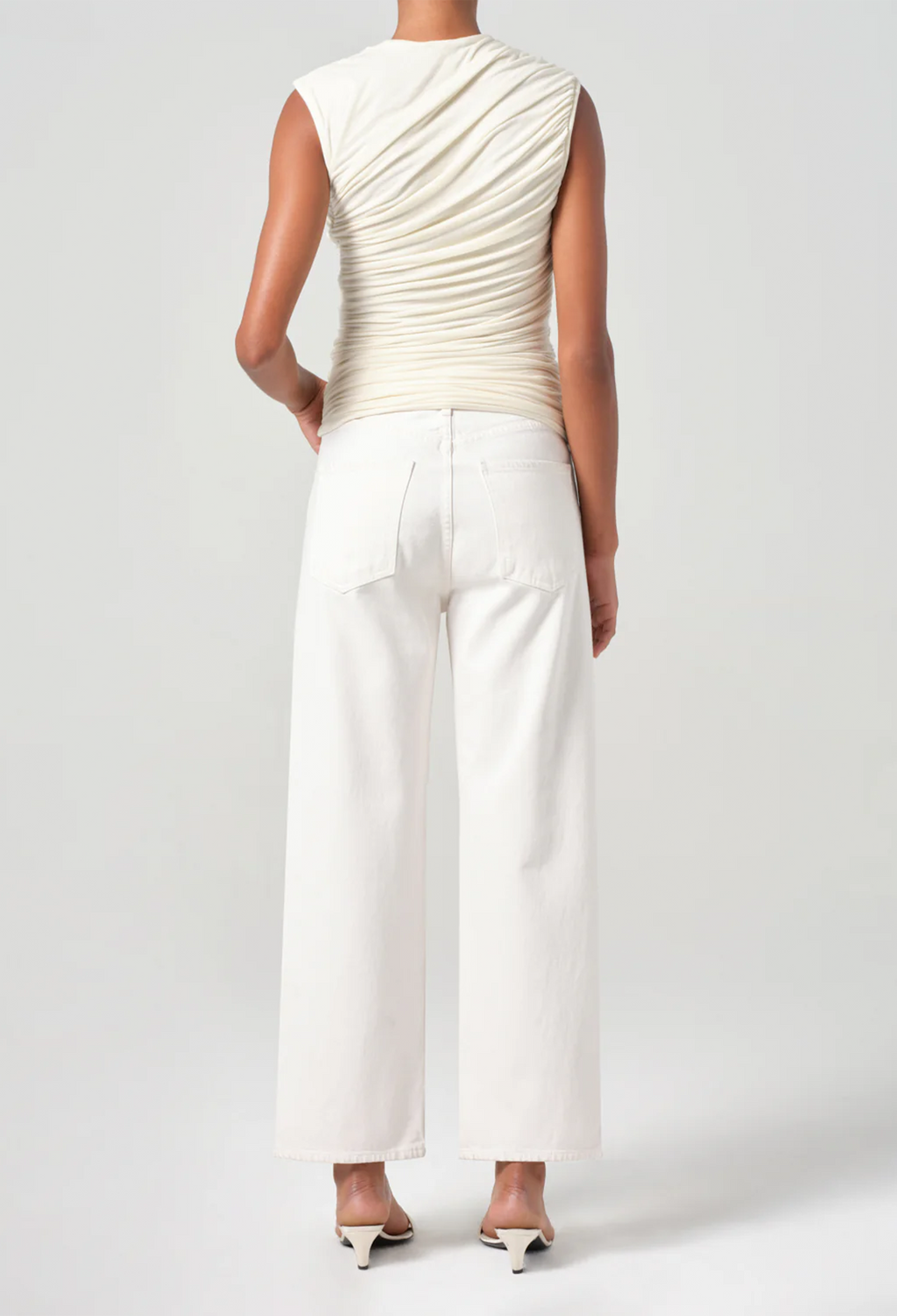 Person wearing a cream sleeveless top and white pants on a plain background
