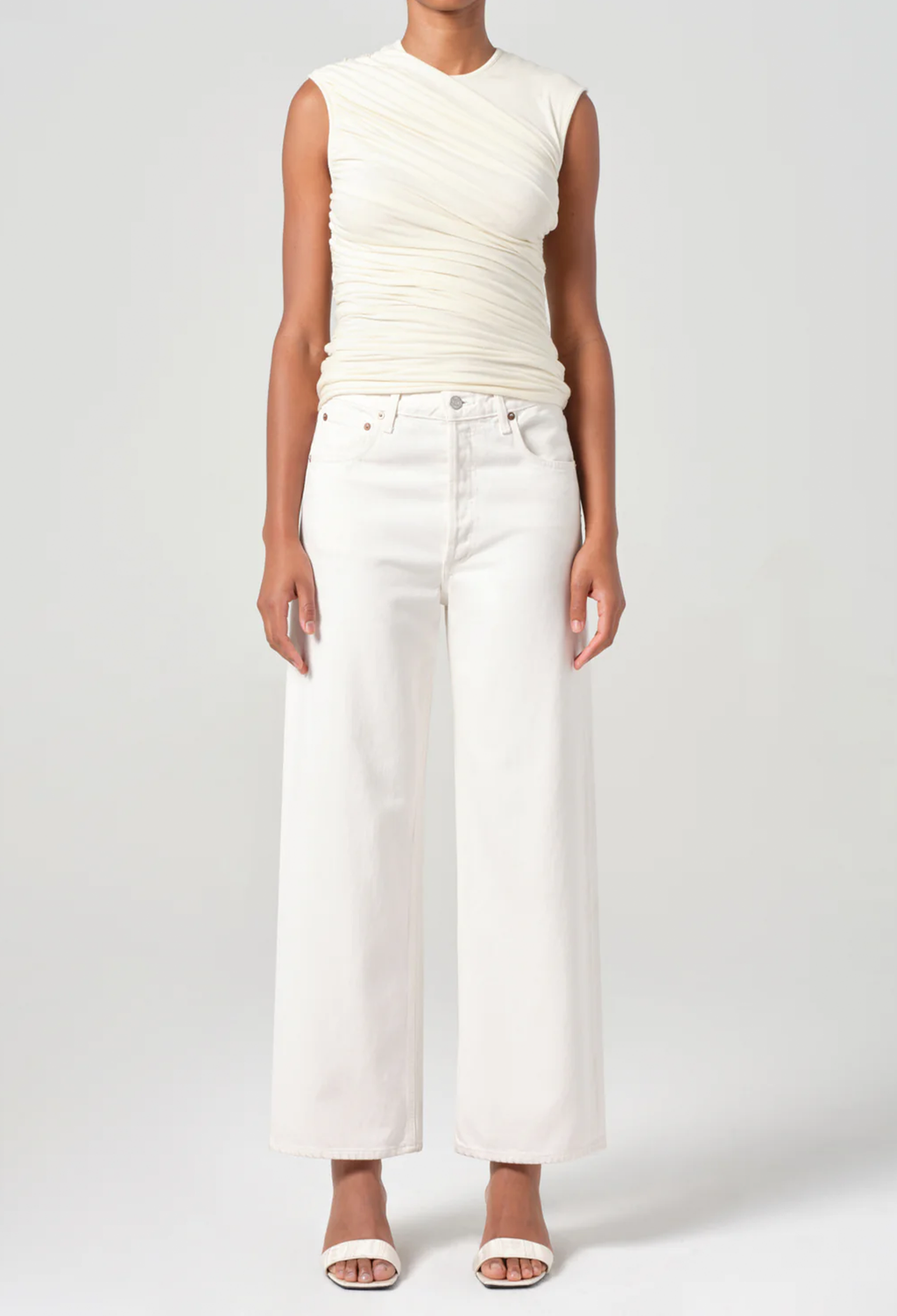 Person wearing a white sleeveless top and wide-leg pants on a plain background