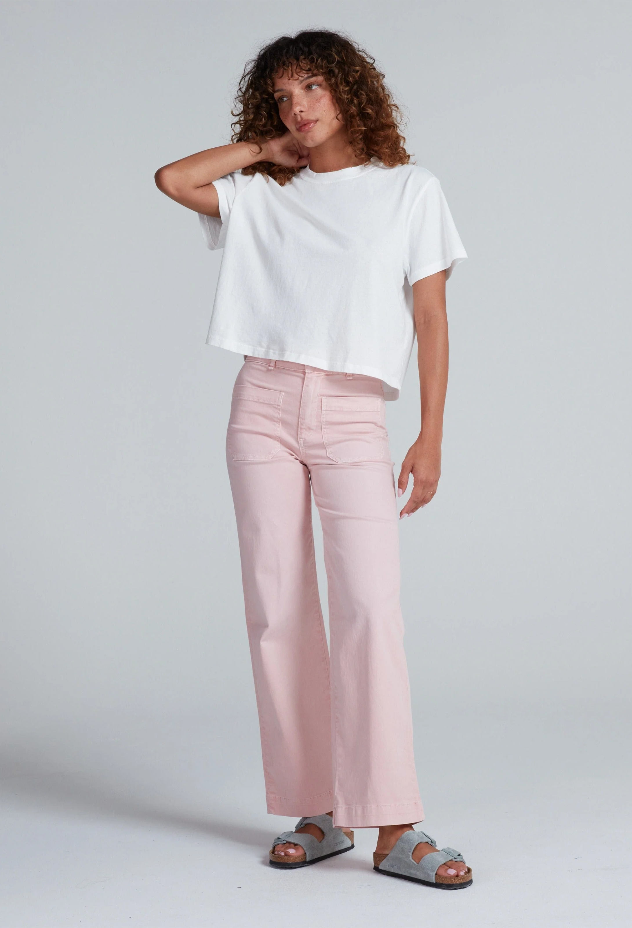 Woman wearing a white top and pink pants on a plain background