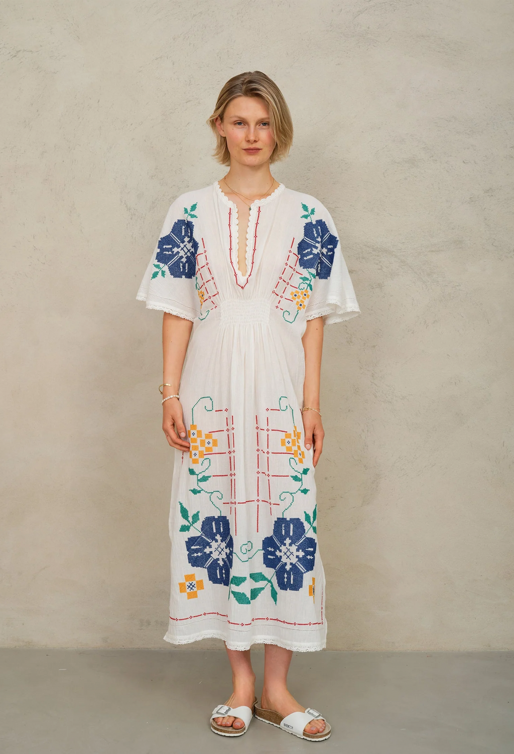 Woman wearing a white dress with colorful floral embroidery against a beige background