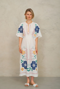 Woman wearing a white dress with colorful floral embroidery against a beige background