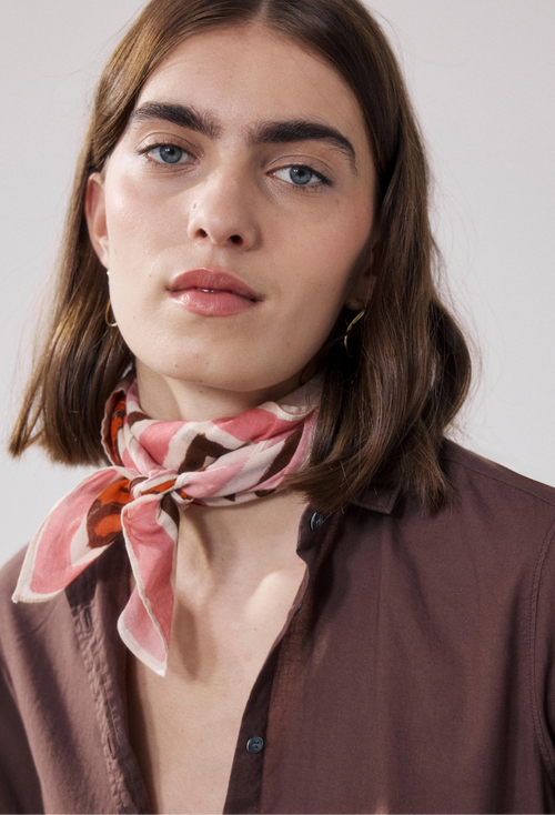 Person wearing a patterned scarf around their neck against a plain background