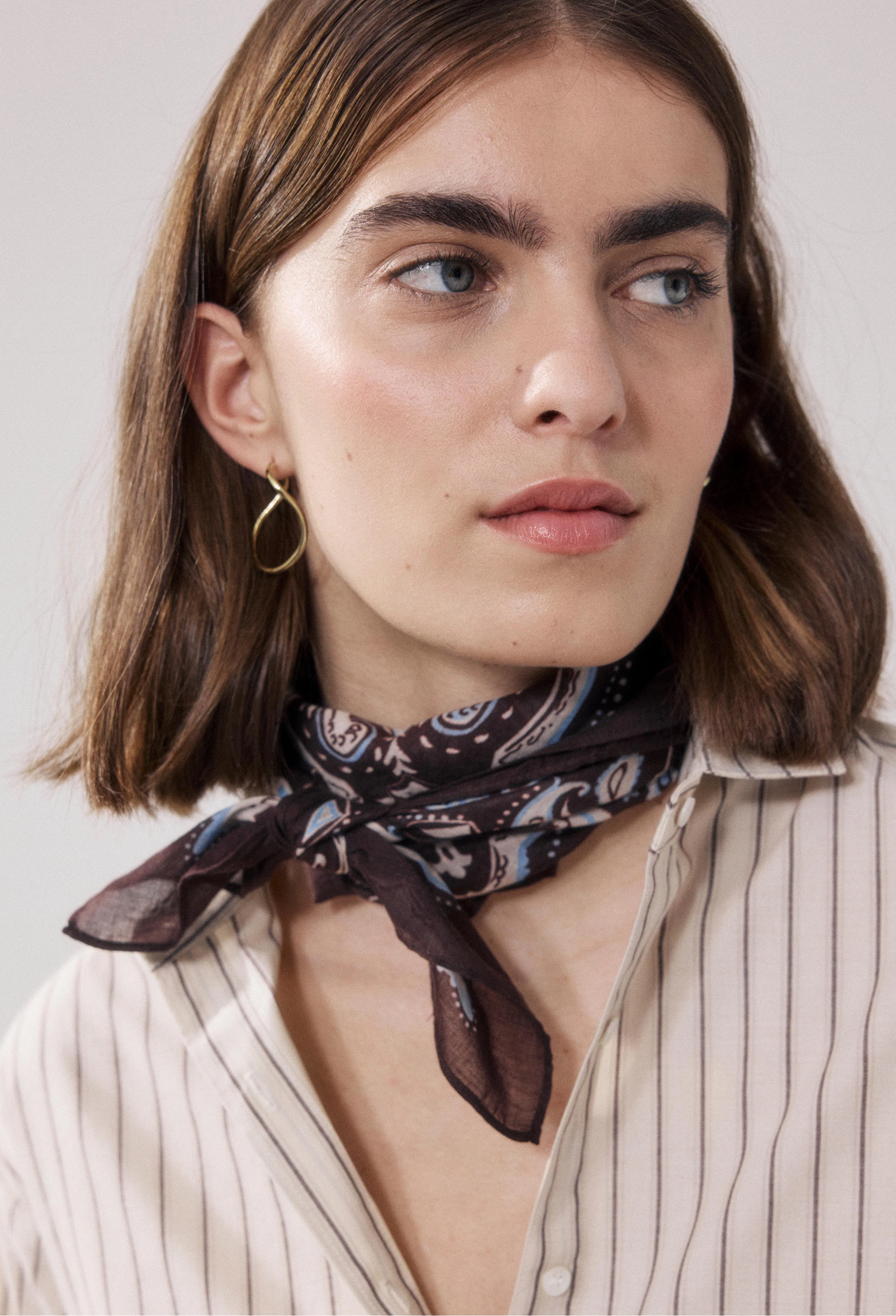 Woman wearing a patterned scarf around her neck against a plain background