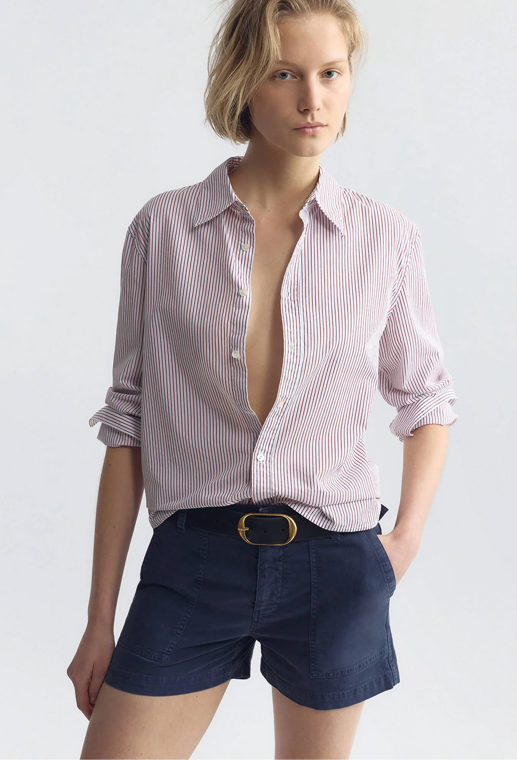Woman wearing a red and white striped shirt with rolled-up sleeves and navy shorts on a white background