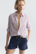 Woman wearing a red and white striped shirt with rolled-up sleeves and navy shorts on a white background