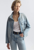 Woman wearing a light blue denim jacket and jeans on a white background