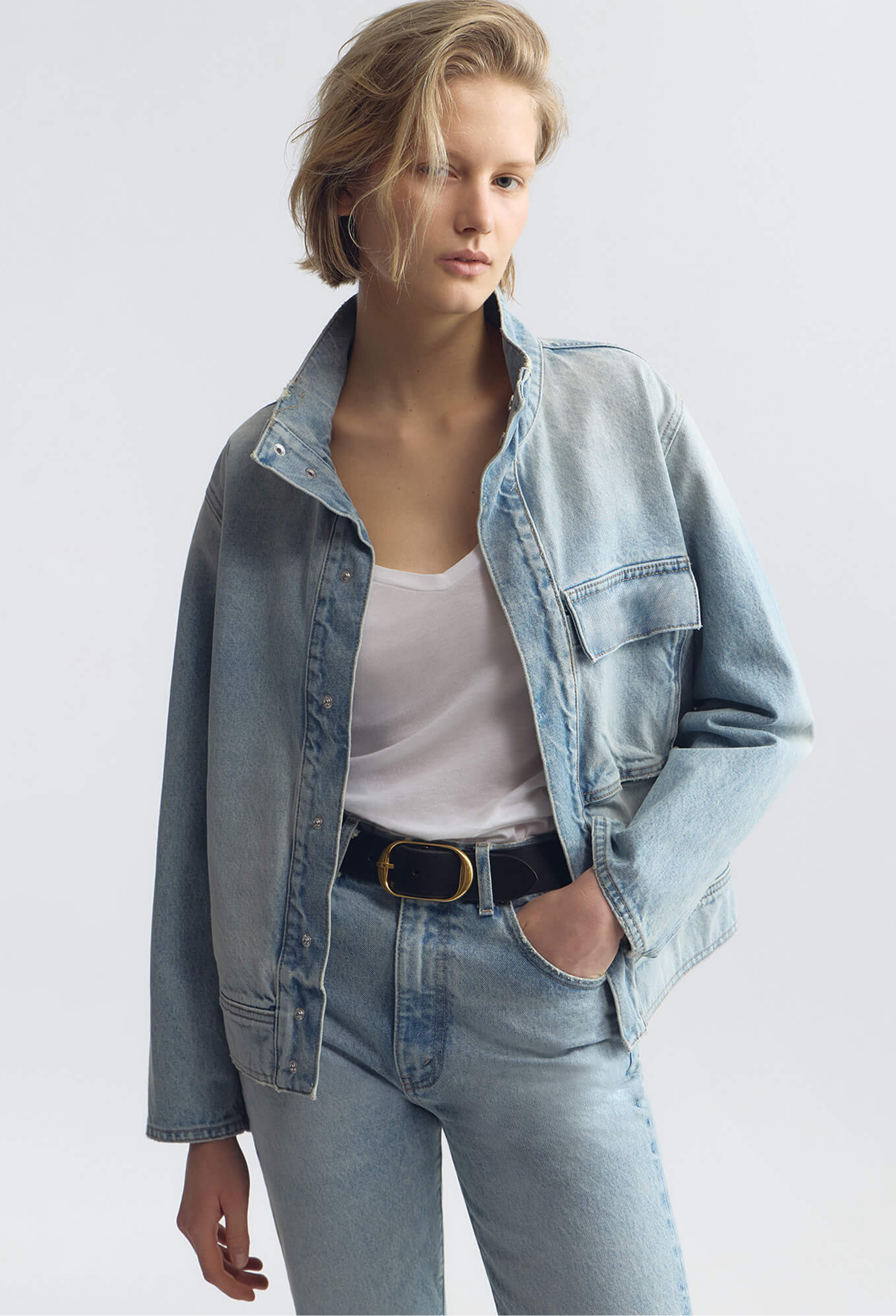 Woman wearing a light blue denim jacket and jeans on a white background
