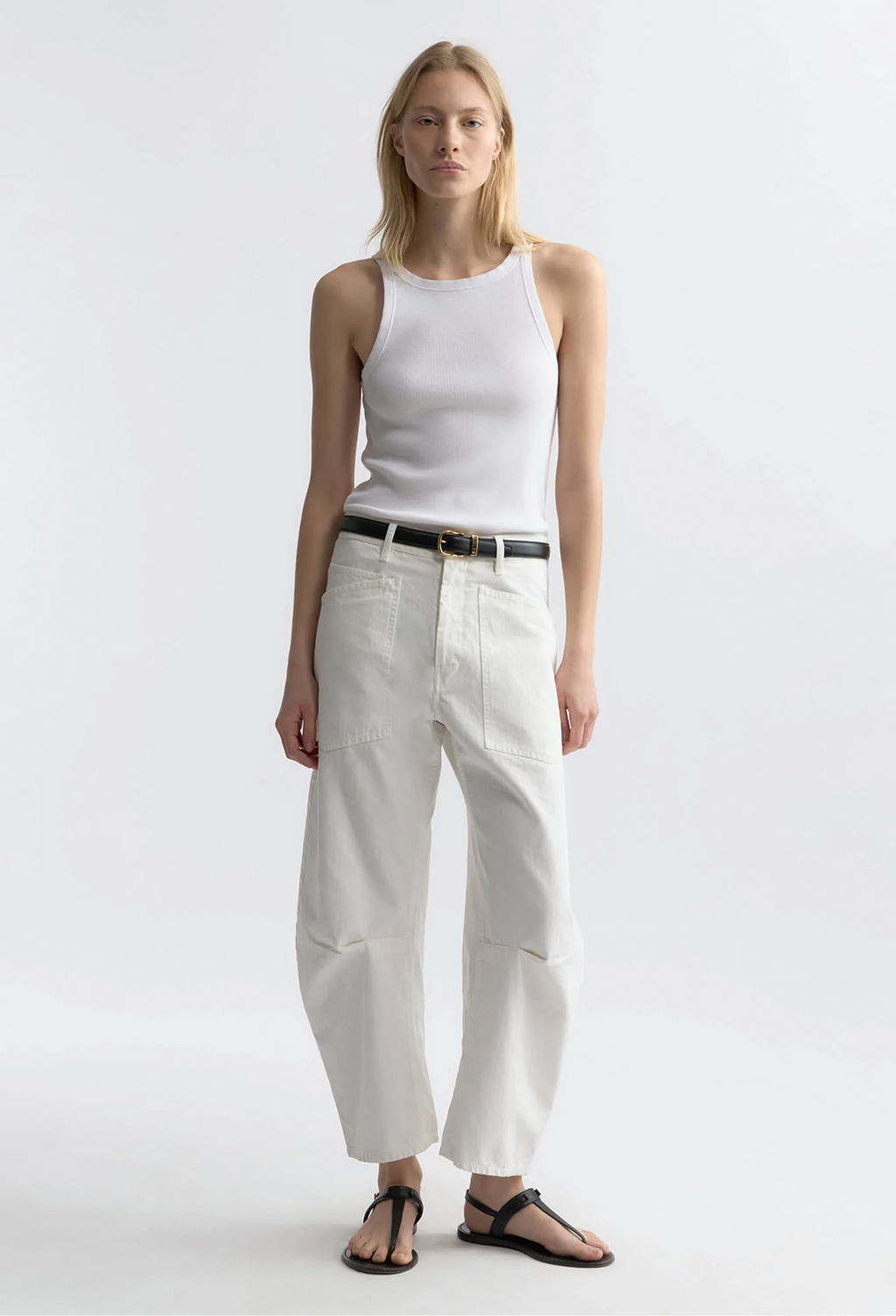 Woman wearing a white sleeveless top and white pants on a plain background