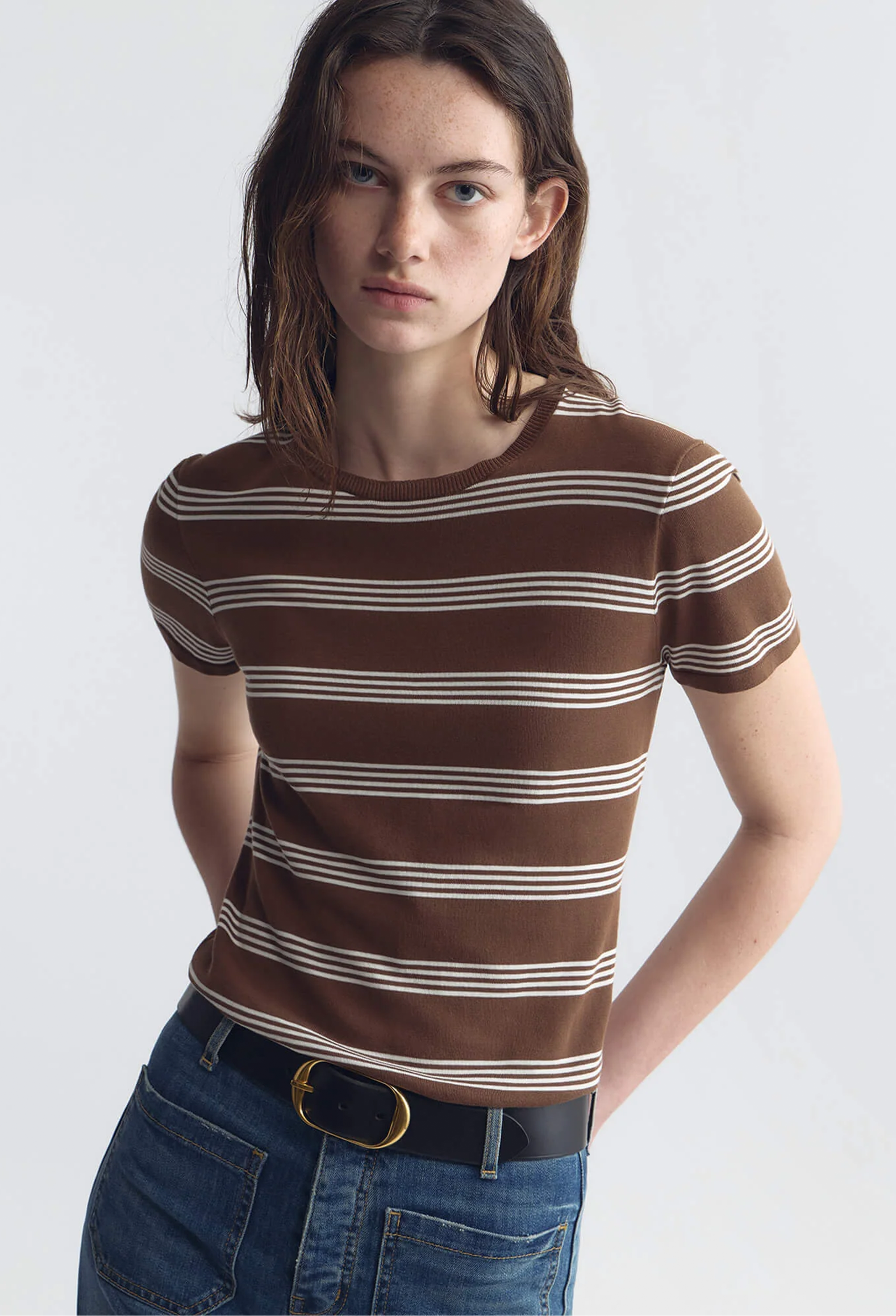Woman wearing a brown and white striped shirt with blue jeans on a white background